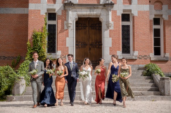 Bride groom bridesmaids and groomsmen walk in the sunshine together